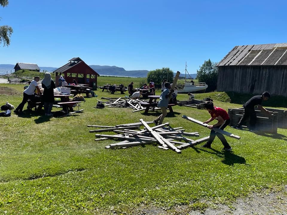  A group of people are working together to build a wooden structure in a field. In the background, there is a red house and a barn. The image represents the search query 'Safe meeting place for first date' because it shows a group of people in a safe and public space.